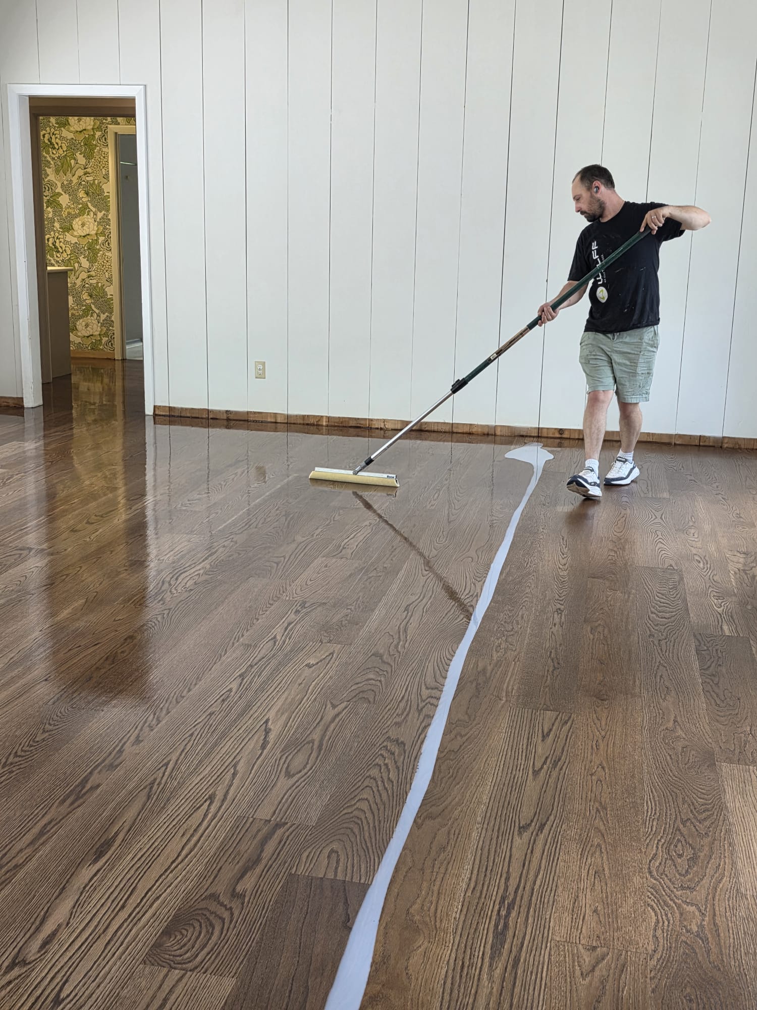 A Georgia Real Floors craftsman applying a finish coat to a refinished white oak floor in a residential home